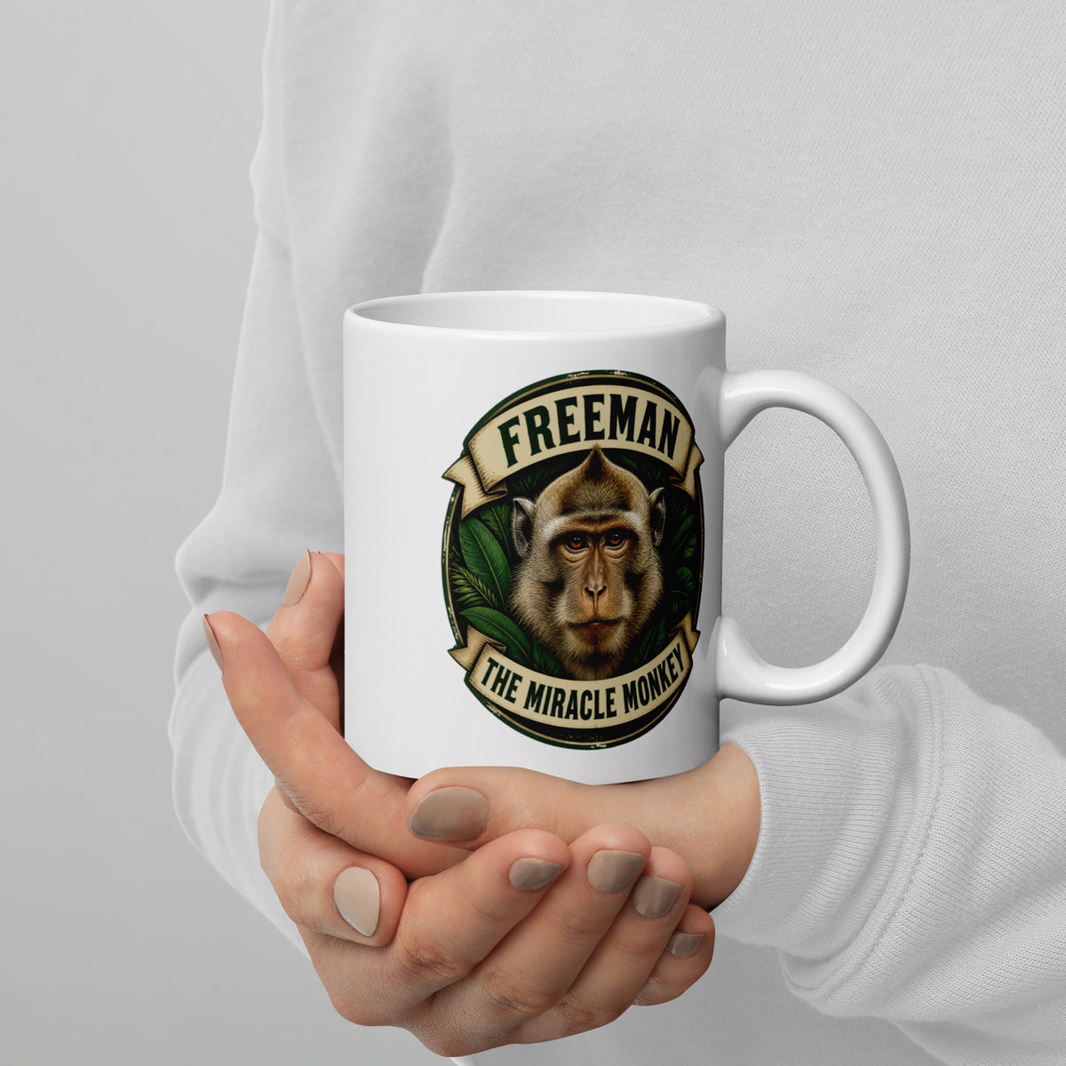 Hvidt keramikkrus med Freeman The Miracle Monkey badge med en abe i grønt, holdt i hænderne, hank til højre