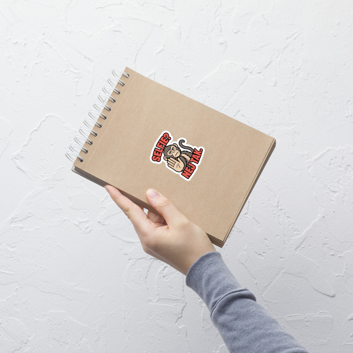 Klistermærke med teksten Selfie? Nej tak og en abe der holder hånden op, 7,5 x 7,5 cm, på en notesbog