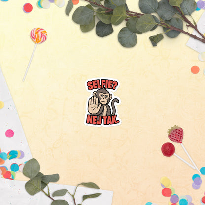 Klistermærke med teksten Selfie? Nej tak og en abe der holder hånden op, 7,5 x 7,5 cm, på en lys baggrund med blomster