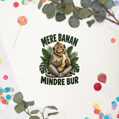 Klistermærke med teksten Mere banan, mindre bur og en glad abe med en banan, 14 x 14 cm, på en hvid baggrund med blomster