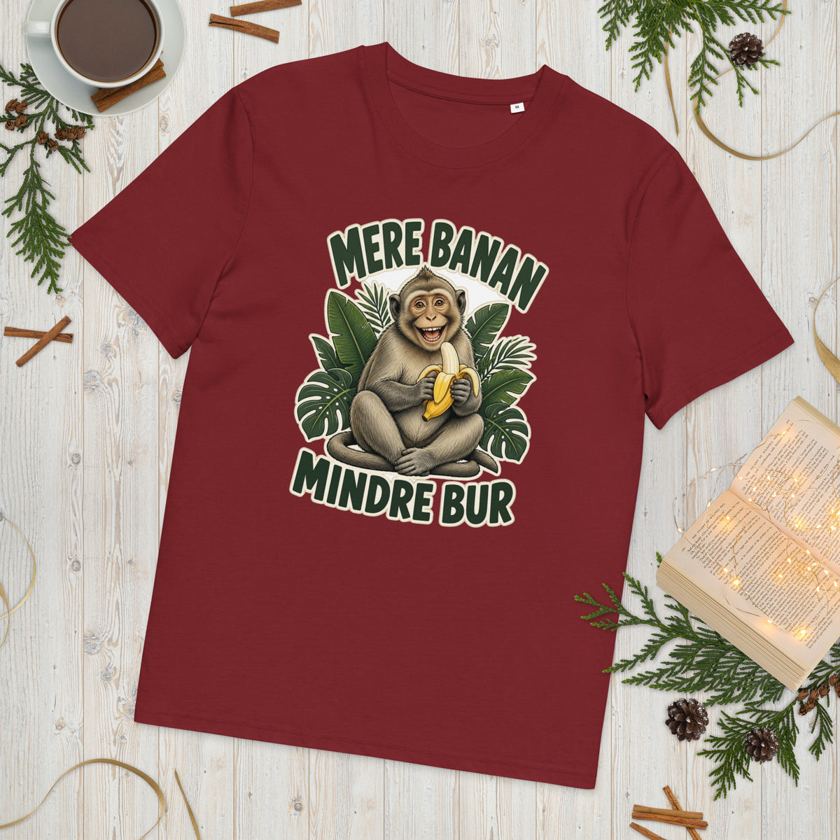 Abe t-shirt med teksten Mere banan, mindre bur i farven bordeaux, lagt på et lyst træbord