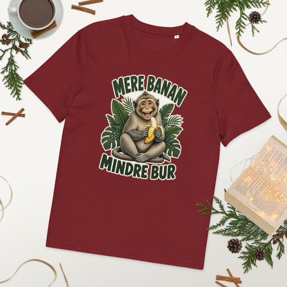 Abe t-shirt med teksten Mere banan, mindre bur i farven bordeaux, lagt på et bord med kaffe og grønt