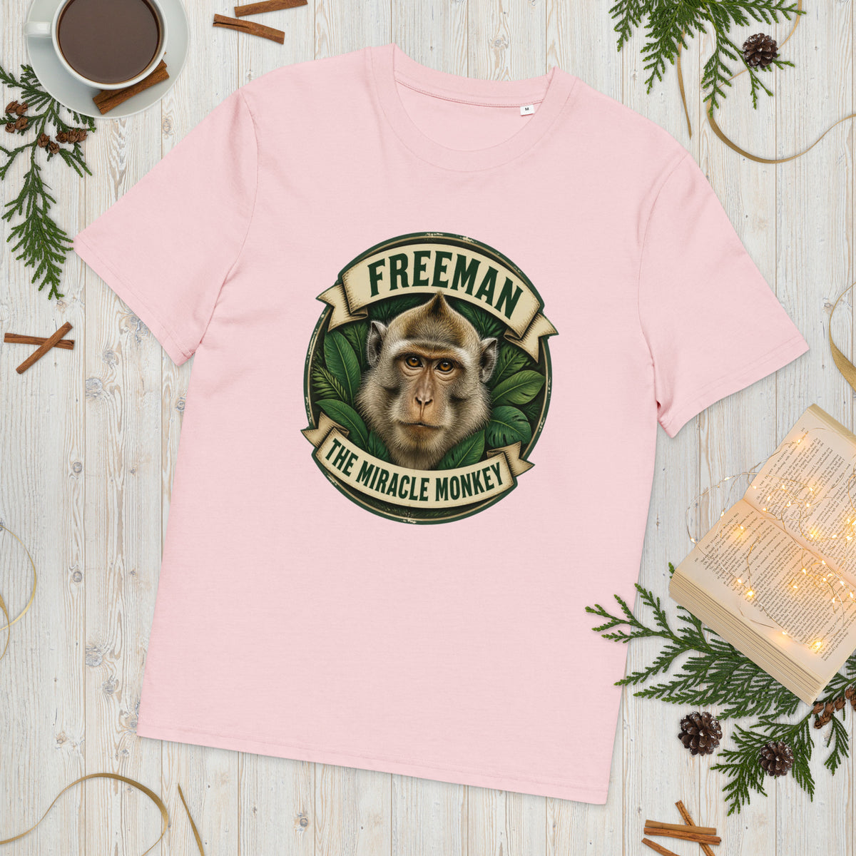 Freeman The Miracle Monkey t-shirt med abe i grønt badge i farven lyserød, lagt på et lyst træbord