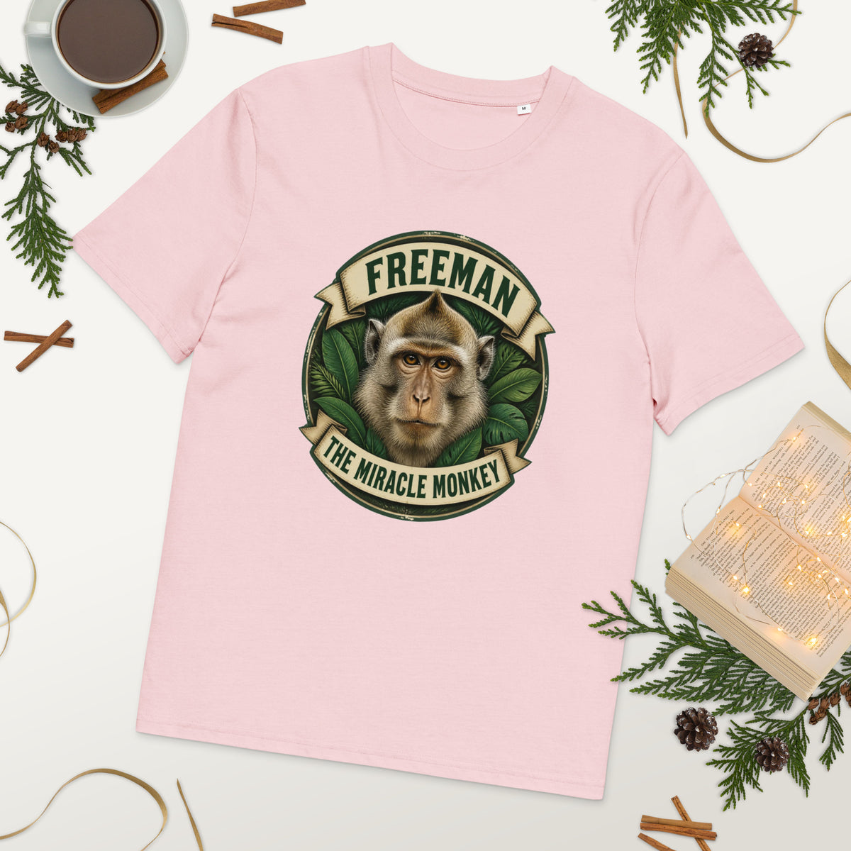 Freeman The Miracle Monkey t-shirt med abe i grønt badge i farven lyserød, lagt på et bord med kaffe og grønt