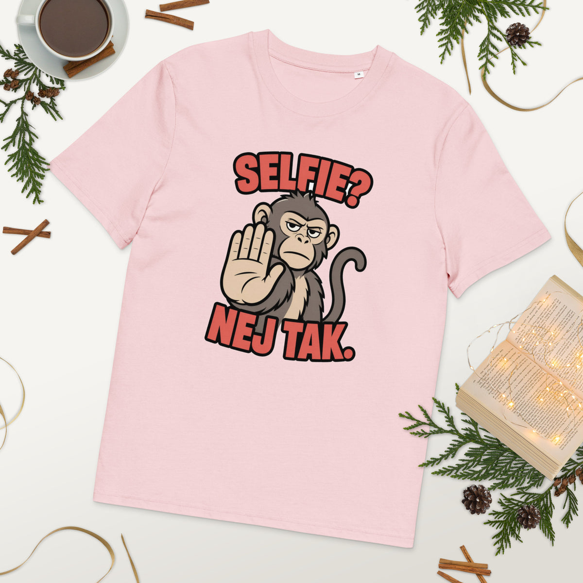 Sjov abe t-shirt med teksten Selfie? Nej tak. i farven lyserød, lagt på et bord med kaffe og grønt