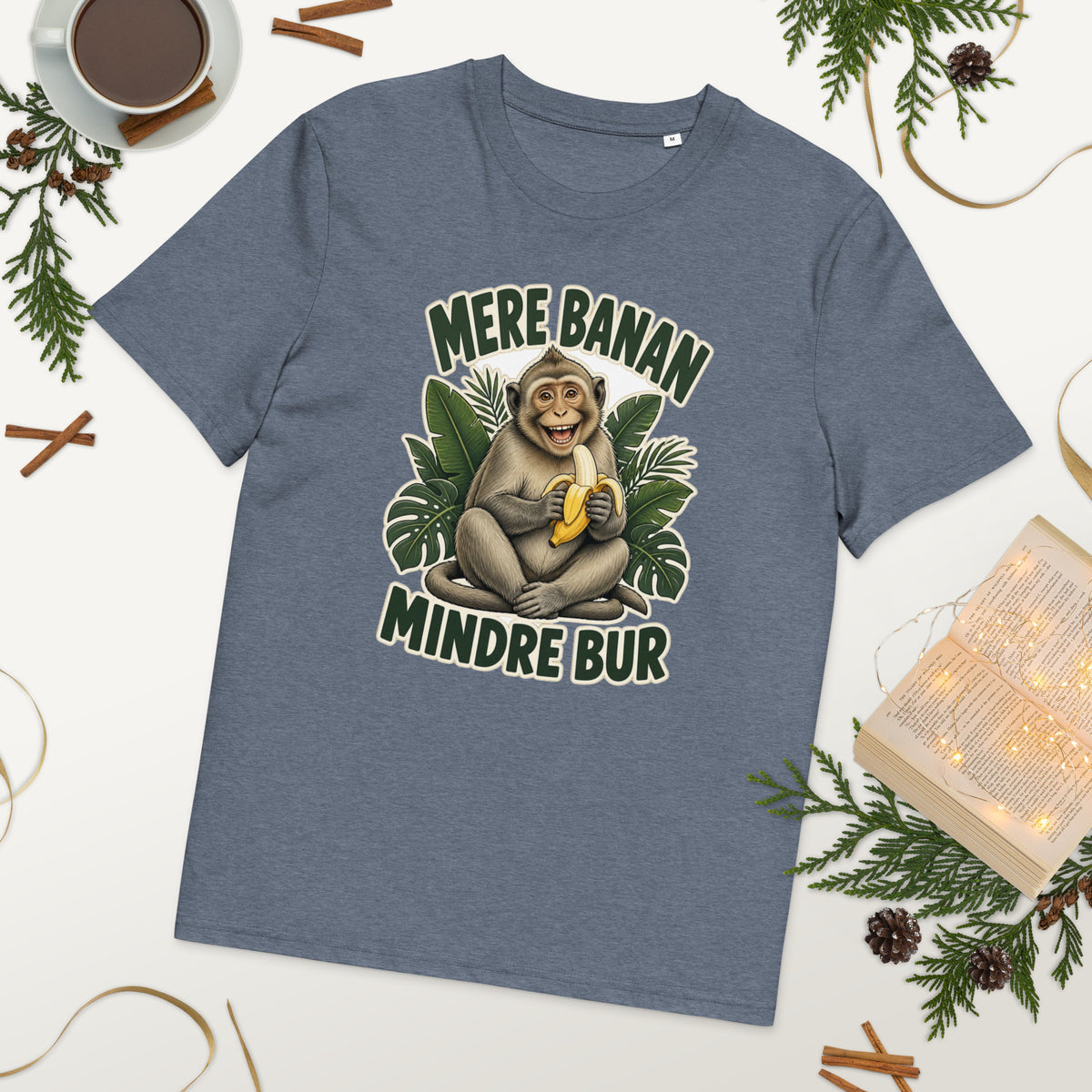 Abe t-shirt med teksten Mere banan, mindre bur i farven blågrå meleret, lagt på et bord med kaffe og grønt