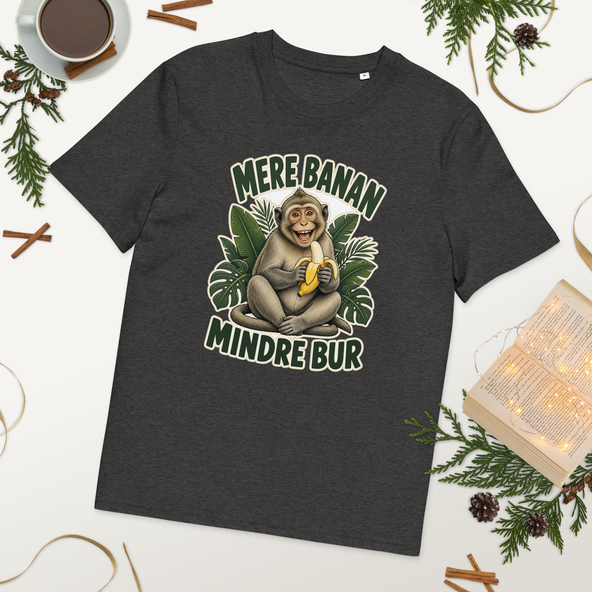 Abe t-shirt med teksten Mere banan, mindre bur i farven mørkegrå meleret, lagt på et bord med kaffe og grønt