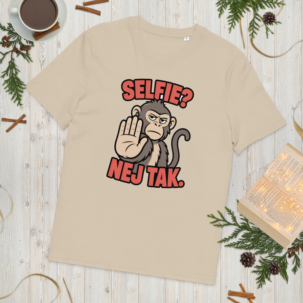 Sjov abe t-shirt med teksten Selfie? Nej tak. i farven sand, lagt på et lyst træbord