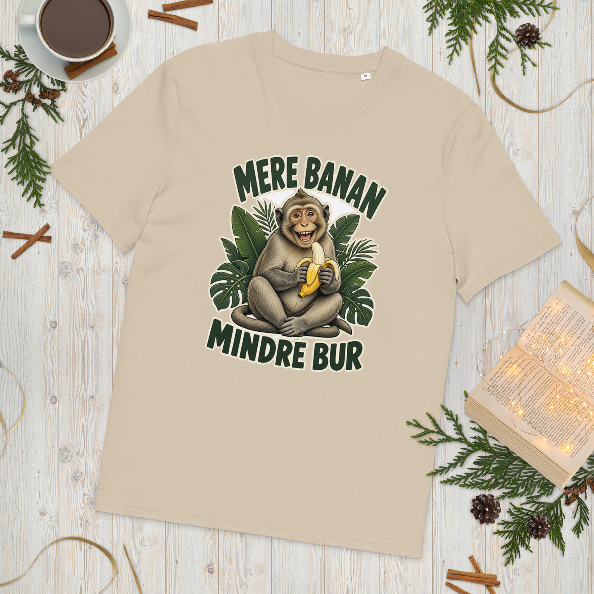 Abe t-shirt med teksten Mere banan, mindre bur i farven sand, lagt på et lyst træbord