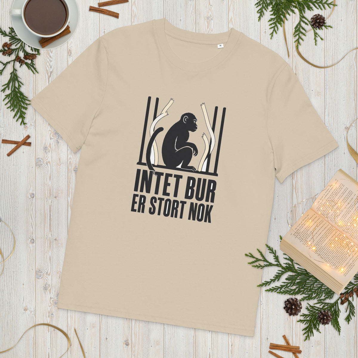T-shirt med teksten Intet bur er stort nok i farven sand, lagt på et lyst træbord