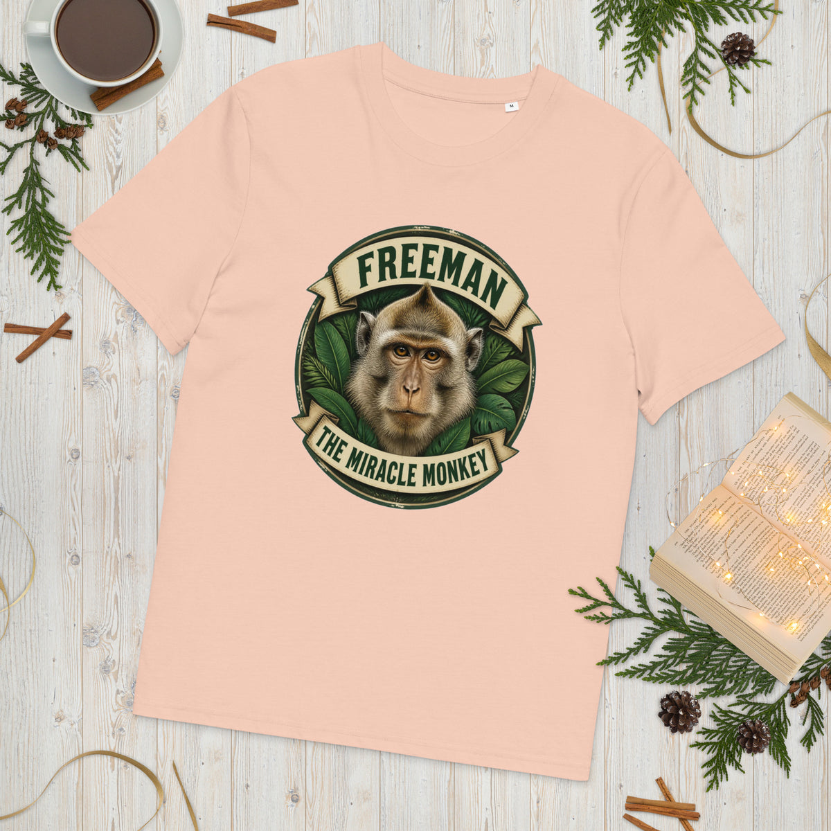 Freeman The Miracle Monkey t-shirt med abe i grønt badge i farven fersken, lagt på et lyst træbord