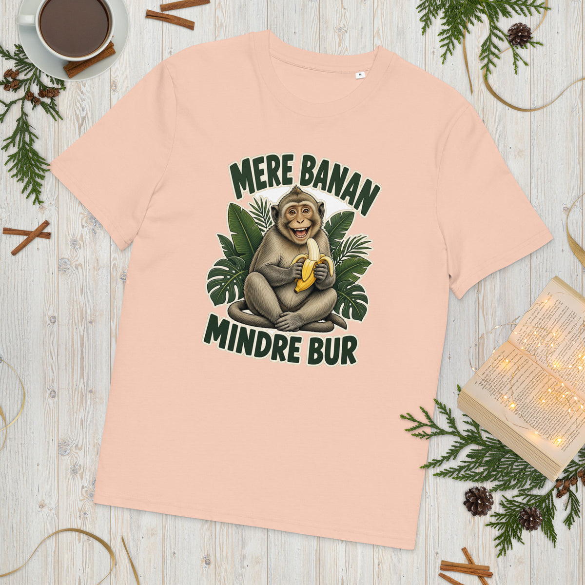 Abe t-shirt med teksten Mere banan, mindre bur i farven fersken, lagt på et lyst træbord