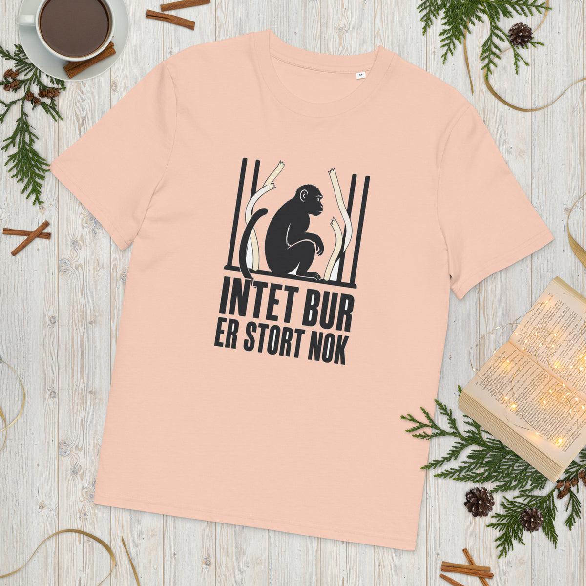 T-shirt med teksten Intet bur er stort nok i farven fersken, lagt på et lyst træbord