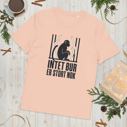 T-shirt med teksten Intet bur er stort nok i farven fersken, lagt på et lyst træbord