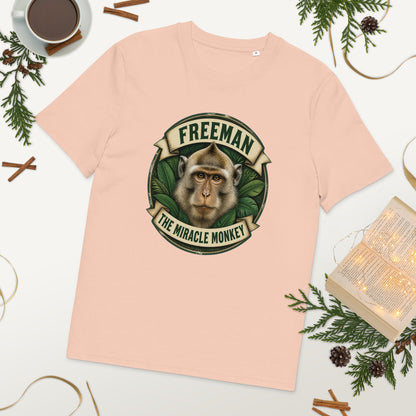 Freeman The Miracle Monkey t-shirt med abe i grønt badge i farven fersken, lagt på et bord med kaffe og grønt
