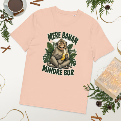 Abe t-shirt med teksten Mere banan, mindre bur i farven fersken, lagt på et bord med kaffe og grønt