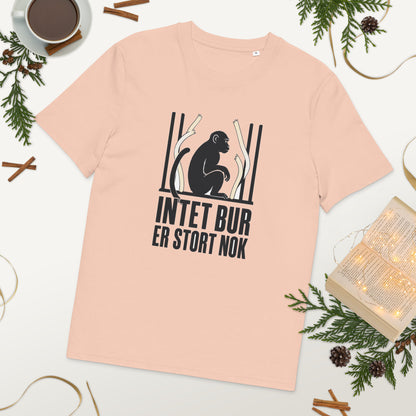 T-shirt med teksten Intet bur er stort nok i farven fersken, lagt på et bord med kaffe og grønt