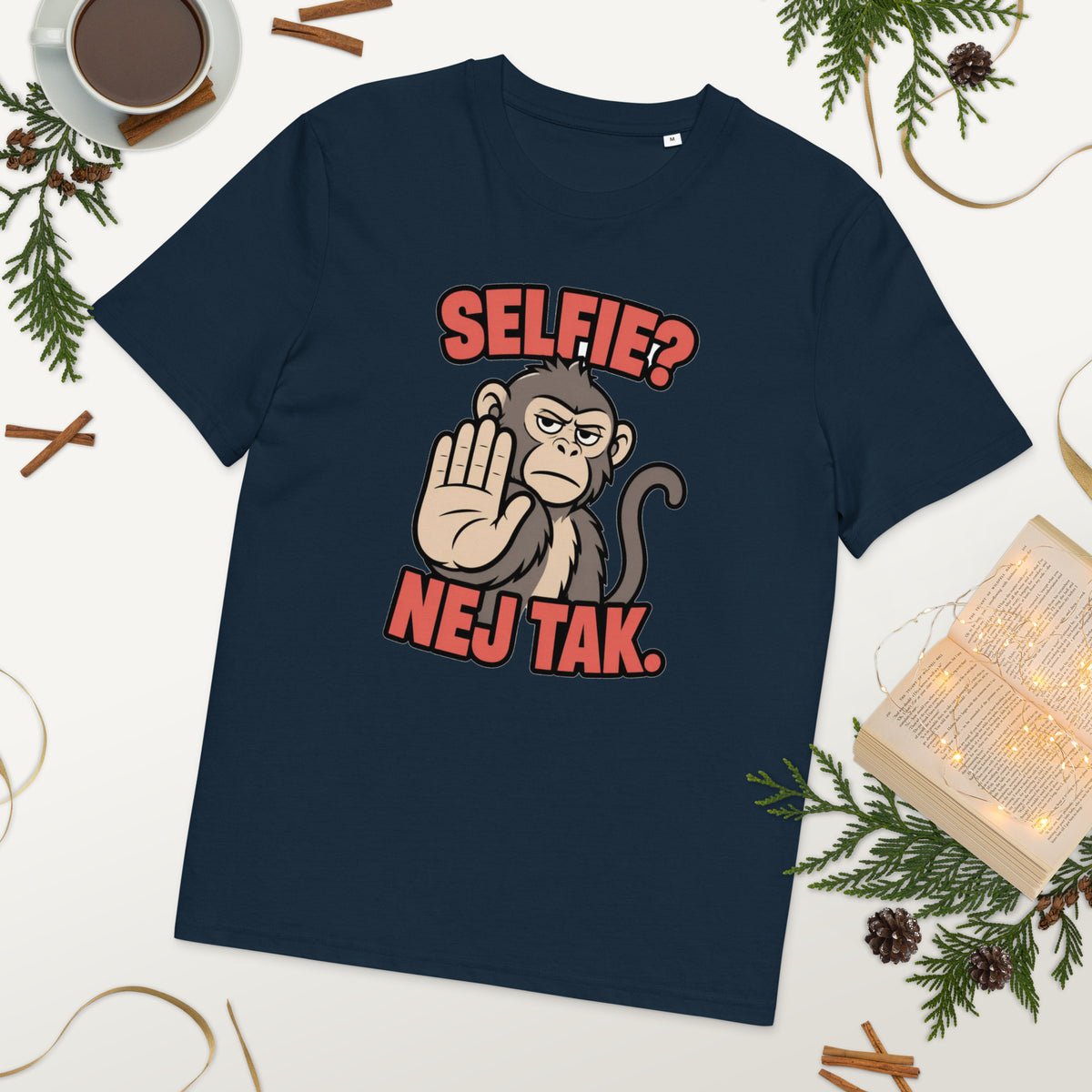 Sjov abe t-shirt med teksten Selfie? Nej tak. i farven marineblå, lagt på et bord med kaffe og grønt