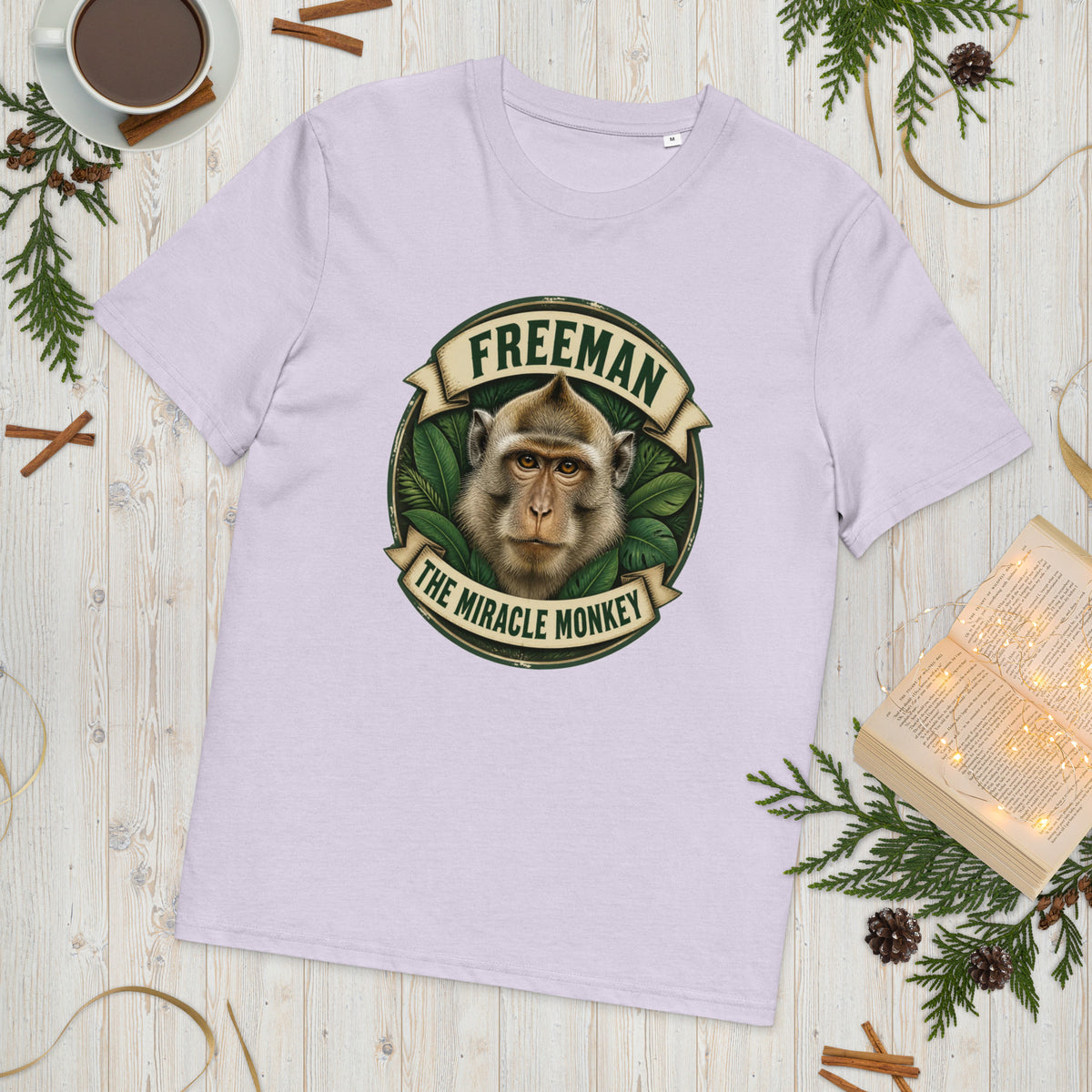 Freeman The Miracle Monkey t-shirt med abe i grønt badge i farven lavendel, lagt på et lyst træbord