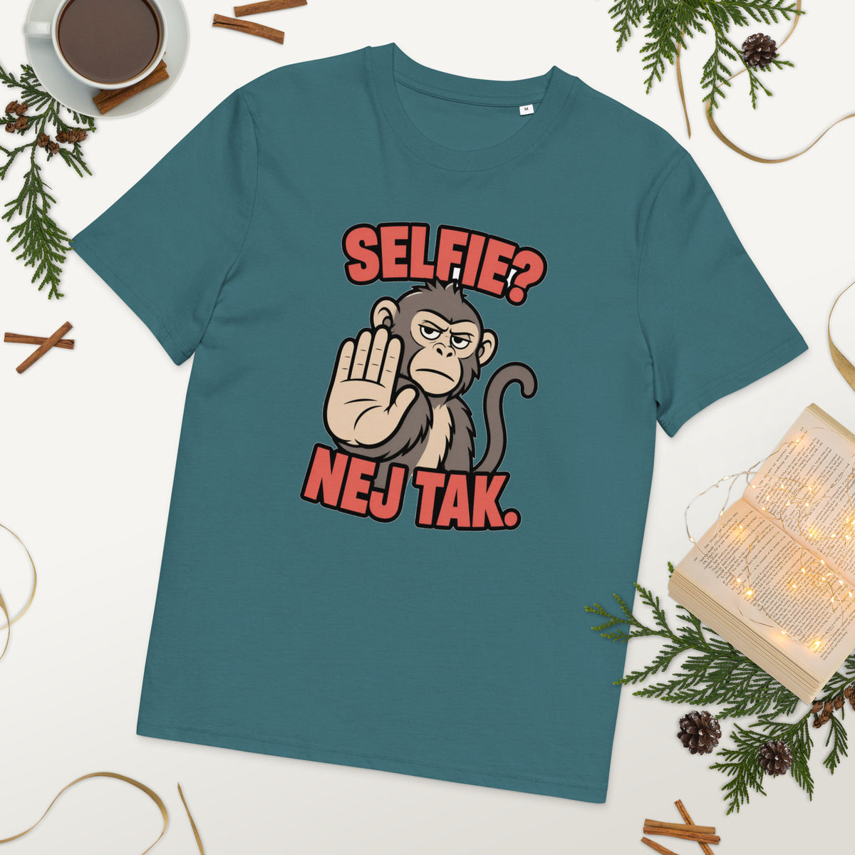 Sjov abe t-shirt med teksten Selfie? Nej tak. i farven petroleumsblå, lagt på et bord med kaffe og grønt