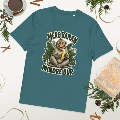 Abe t-shirt med teksten Mere banan, mindre bur i farven petroleumsblå, lagt på et bord med kaffe og grønt