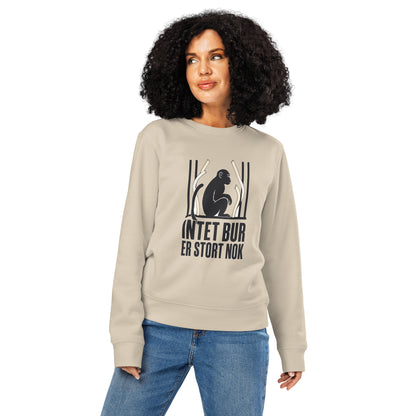 Sweatshirt med teksten Intet bur er stort nok og en abe bag tremmer i farven sand, båret af en ung kvinde