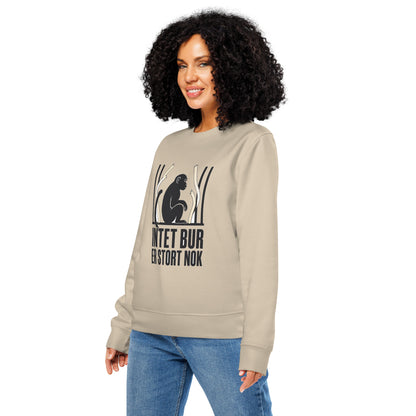 Sweatshirt med teksten Intet bur er stort nok og en abe bag tremmer i farven sand, båret af en ung kvinde, set skråt