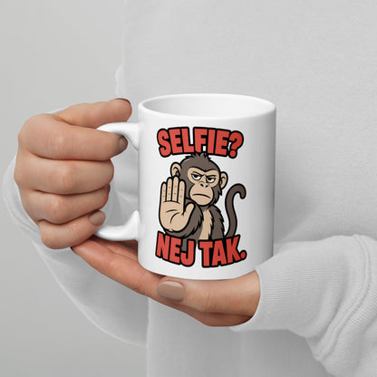 Hvidt keramikkrus med teksten Selfie? Nej tak og en abe der holder hånden op, holdt i hænderne, hank til venstre