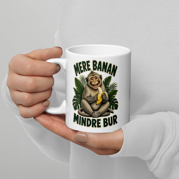 Hvidt keramikkrus med teksten Mere banan, mindre bur og en glad abe med en banan, holdt i hænderne, hank til venstre